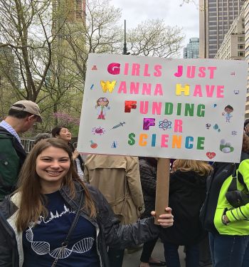 Woman holding up protest sign on street.