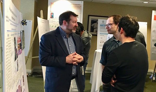 Three men talking in front of a scientific poster.