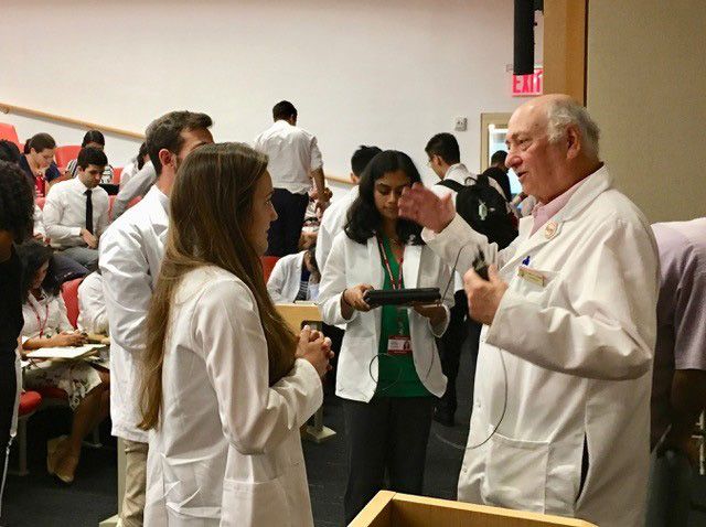 Students wearing lab coats talk with professor.
