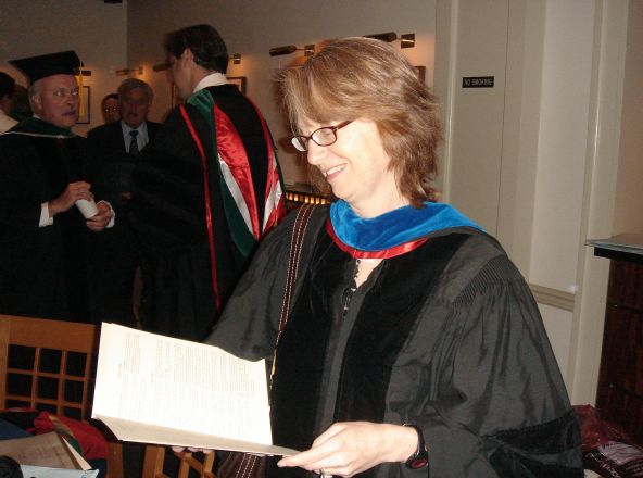 Woman in regalia reading a paper.